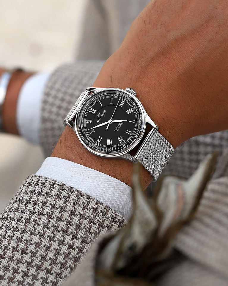 A round Automatic mens watch in Rhodium-plated 316L stainless from Waldor & Co. with black double-layered dial in copper. Curved mineral glass with anti-reflective coating. Miyota 9093 movement. Mesh strap. The model is Continual 39 Amalfi.