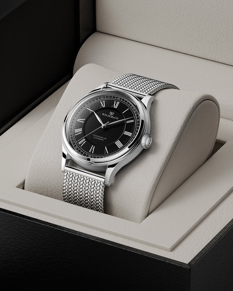 A round Automatic mens watch in Rhodium-plated 316L stainless from Waldor & Co. with black double-layered dial in copper. Curved mineral glass with anti-reflective coating. Miyota 9093 movement. Mesh strap. The model is Continual 39 Amalfi.