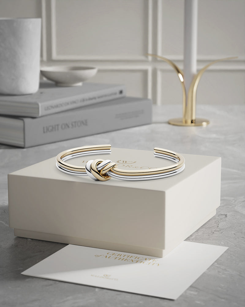 A polished stainless steel bangle in 14k gold from Waldor & Co. One size. The model is Dual Knot Bangle.