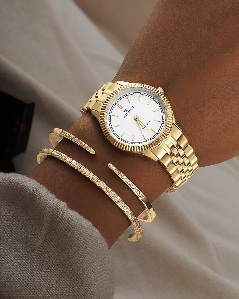 A round womens watch in 22k gold from Waldor & Co. with white sunray dial and a second hand. Seiko movement. The model is Imperial 32 Positano 32mm.